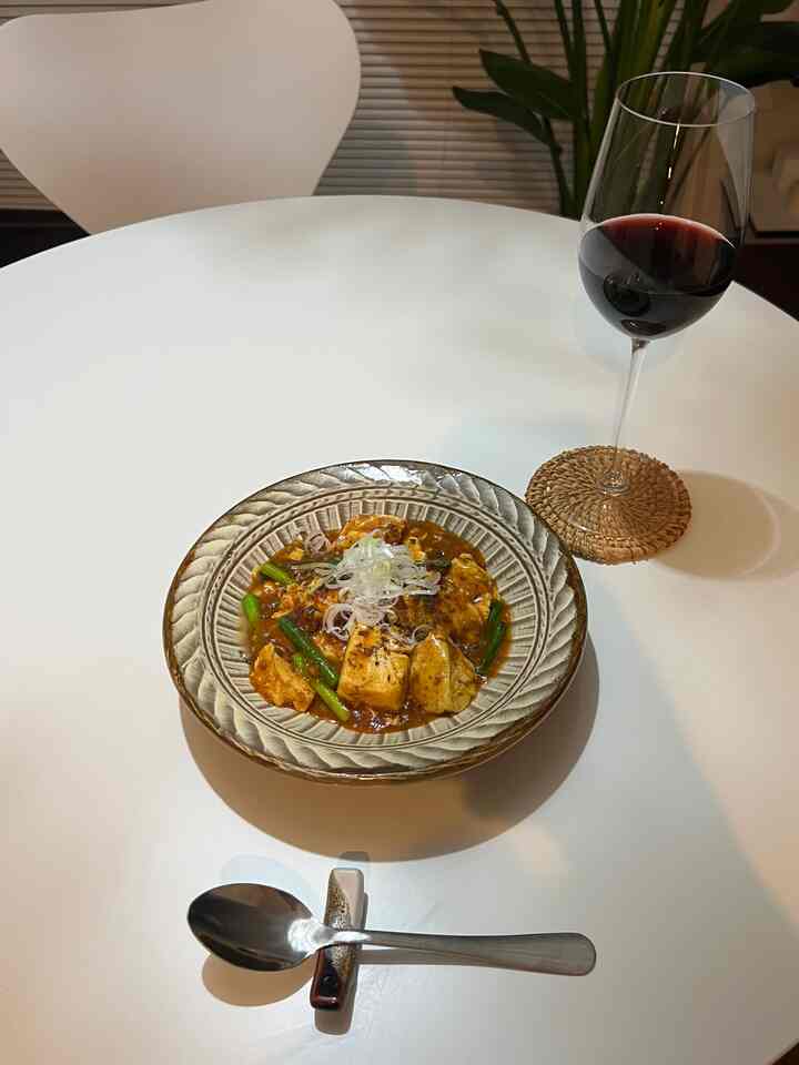 白を基調とした丸テーブルにスプーンとワイングラス、小皿の食事が置かれたシンプルな一人暮らし空間