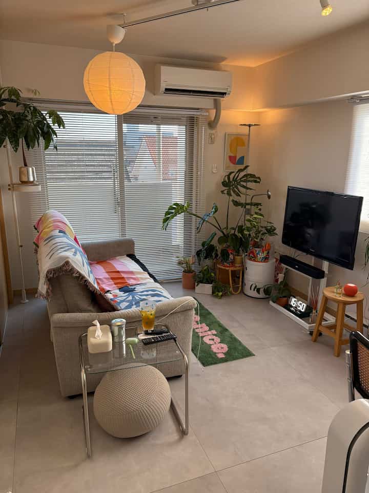 Light beige living room featuring sofa, pendant lighting, and plants creating a cozy mid-century modern atmosphere