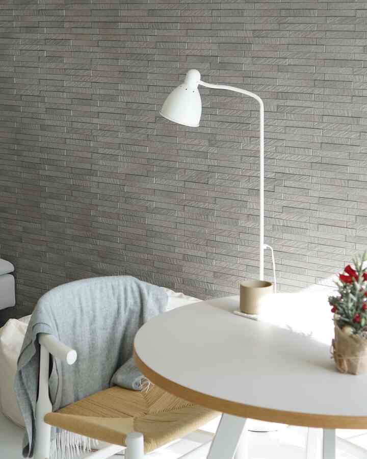 Monotone studio apartment featuring a gray brick wall, white round table, floor lamp, and natural textured chair with simple design