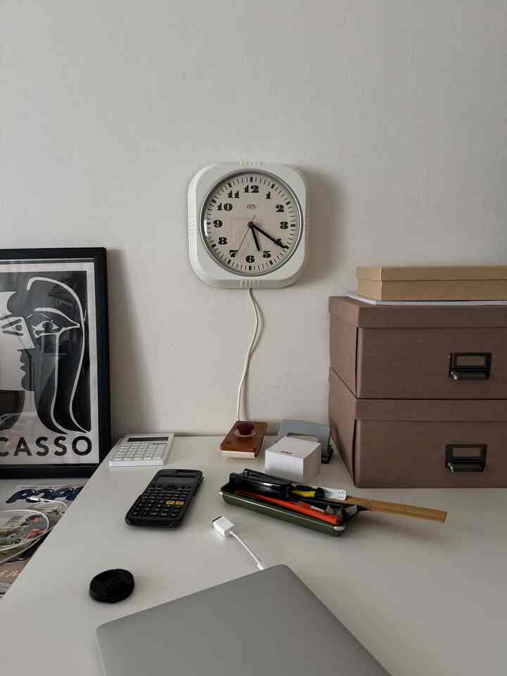 Simple home office space with white wall and desk, featuring retro clock and storage boxes