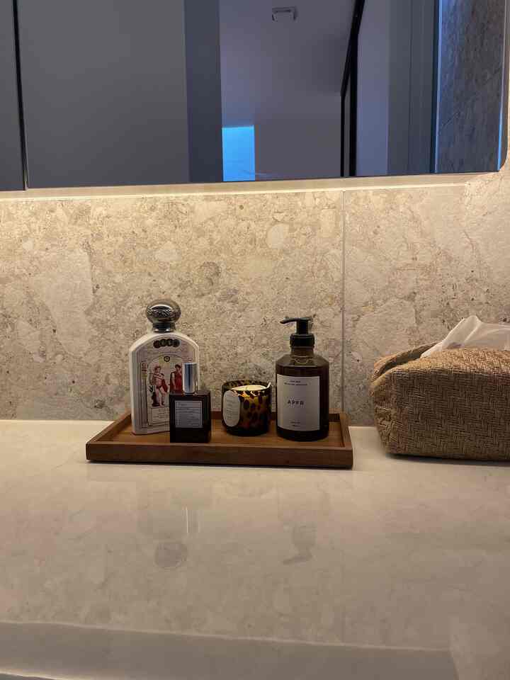 ナチュラルカラーのパウダールーム、縦長の空間に置かれた木製トレイの上にディフューザー、キャンドル、タオルが整った洗面台のある雰囲気のあるインテリア