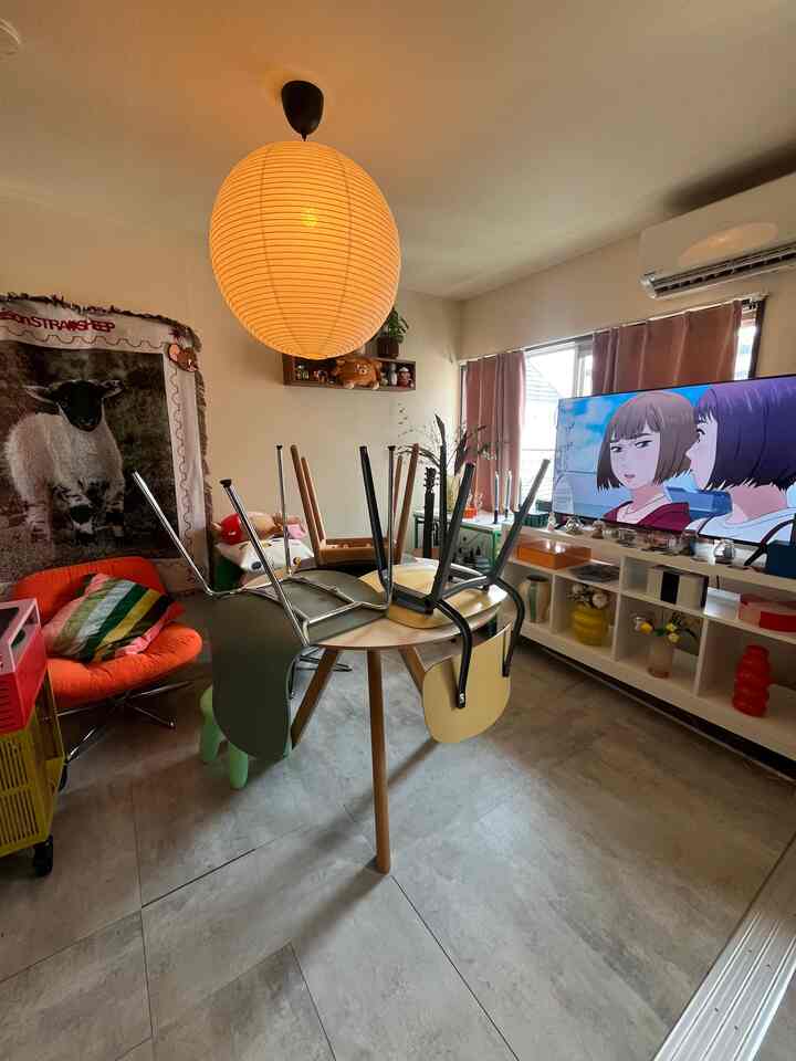 ライトグレーの床がある1LDKのリビング、オレンジのアームチェアと中央のラウンドテーブルが配置されたミッドセンチュリーモダンのインテリア