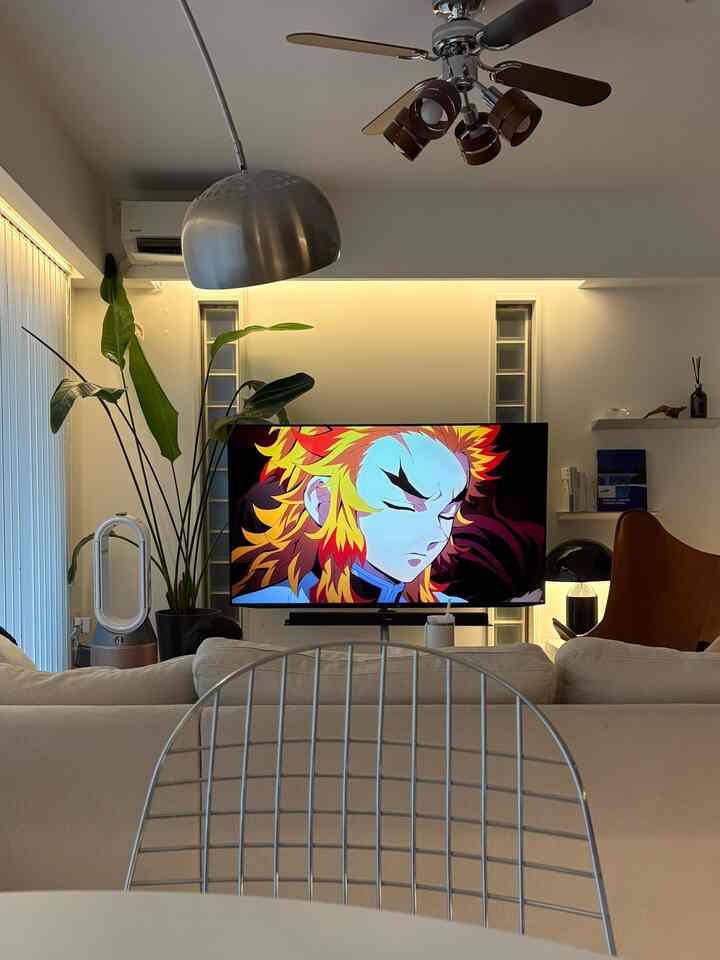 温かみのある色調のリビング、クリーム色のソファとブラウンのレザーアームチェア、大きなテレビと植物が配置されたミッドセンチュリーモダンなインテリア