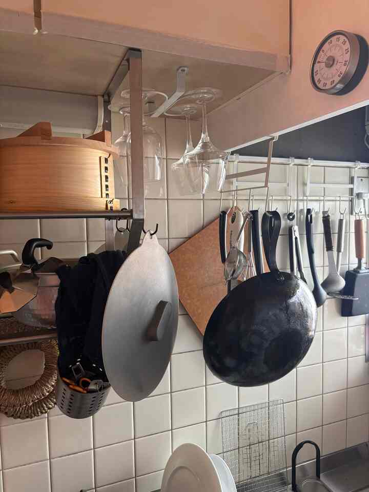 白いタイル壁のキッチン、掛けられたフライパンと様々な調理器具が配置された雰囲気のある空間