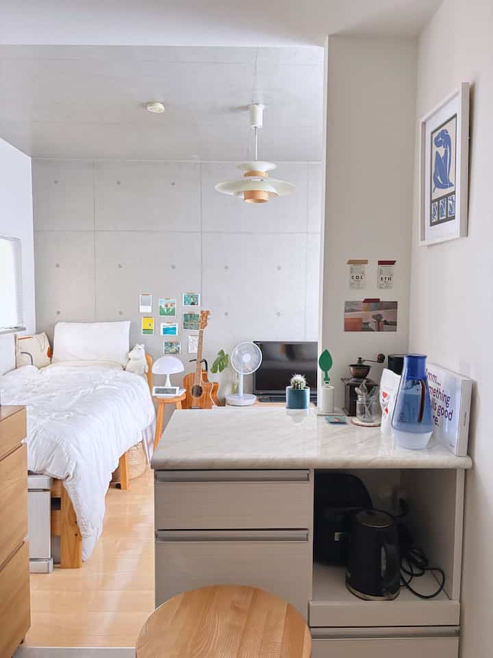 白と木目調のナチュラルモダンなワンルーム、中央に大理石のキッチンカウンターと整然とした寝室が配置された印象的な空間