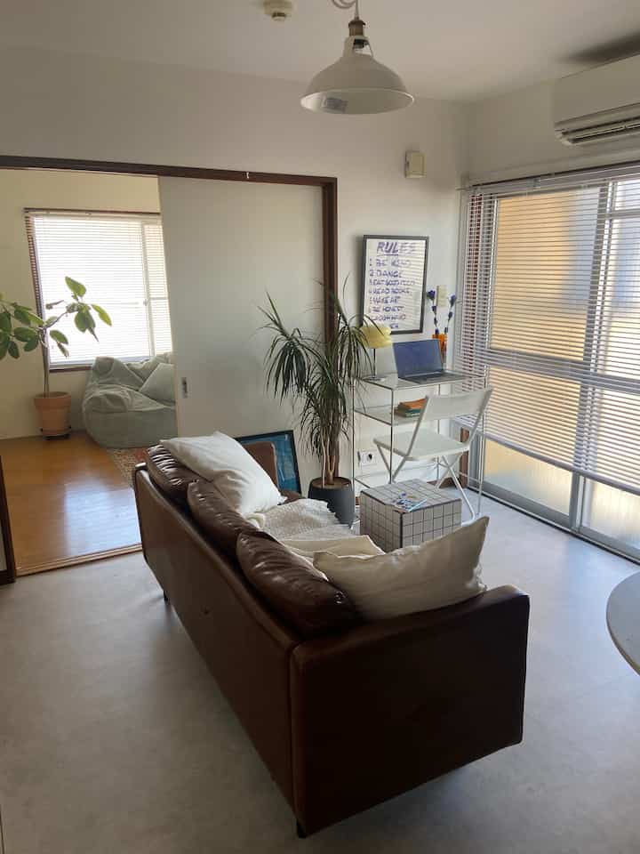 White and brown toned 1DK living room featuring a brown leather sofa centrally and a desk by the window, creating a clean and cozy space