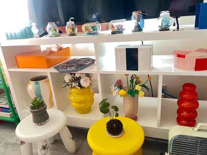 明るい黄色とオレンジの花瓶が並ぶ、清潔感のある白い棚を配したミッドセンチュリーモダンな1LDKのリビング