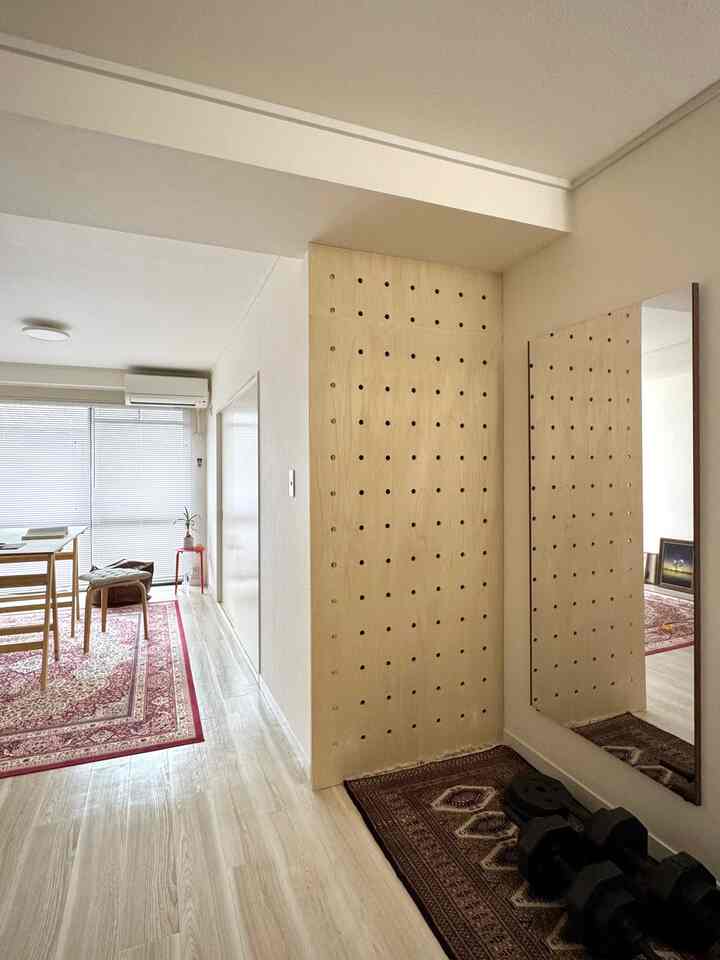 ナチュラルカラーと木目調が調和したリビング・ダイニング、壁に大型の鏡とペグボードが設置された雰囲気のある空間