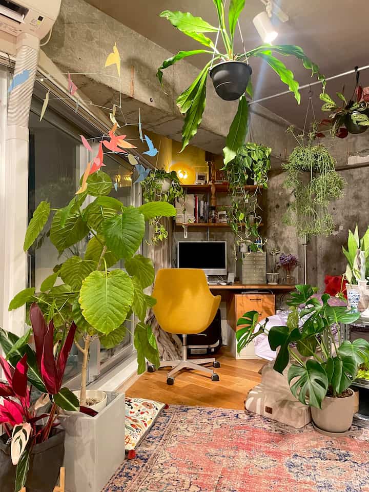 A compact home office filled with lush green plants, featuring a yellow office chair and wood floor in an industrial style interior