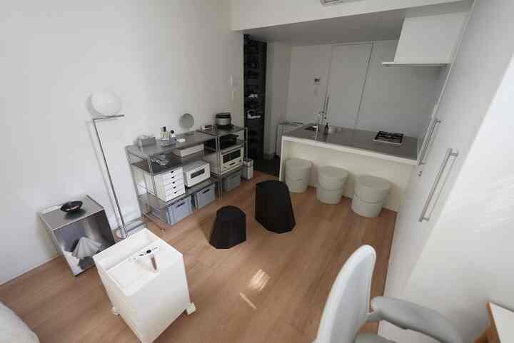 White and wood-toned small kitchen space featuring minimal stools and a stainless steel counter in a simple interior