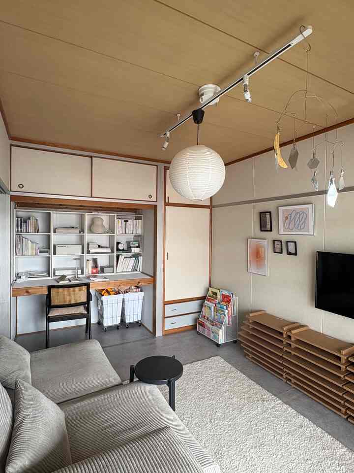 Natural wood-tone ceiling and white walls define a two-person living room featuring sofa and desk in a cozy study area