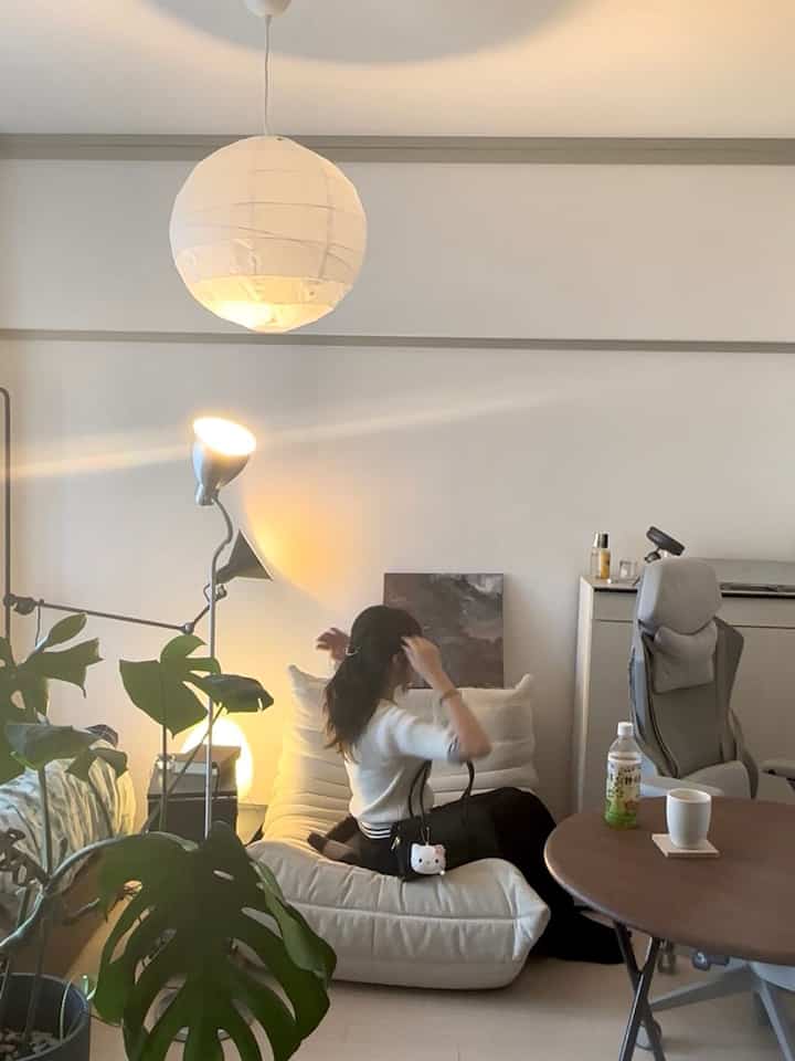 柔らかなベージュ色調の5畳の部屋、白いソファとフロアランプ、大きな観葉植物が配置された落ち着いたインテリア