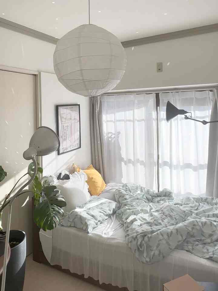 白とナチュラルカラーの狭い寝室、ベッドと枕、カーテン、フロアランプが配置された明るく居心地の良いインテリア