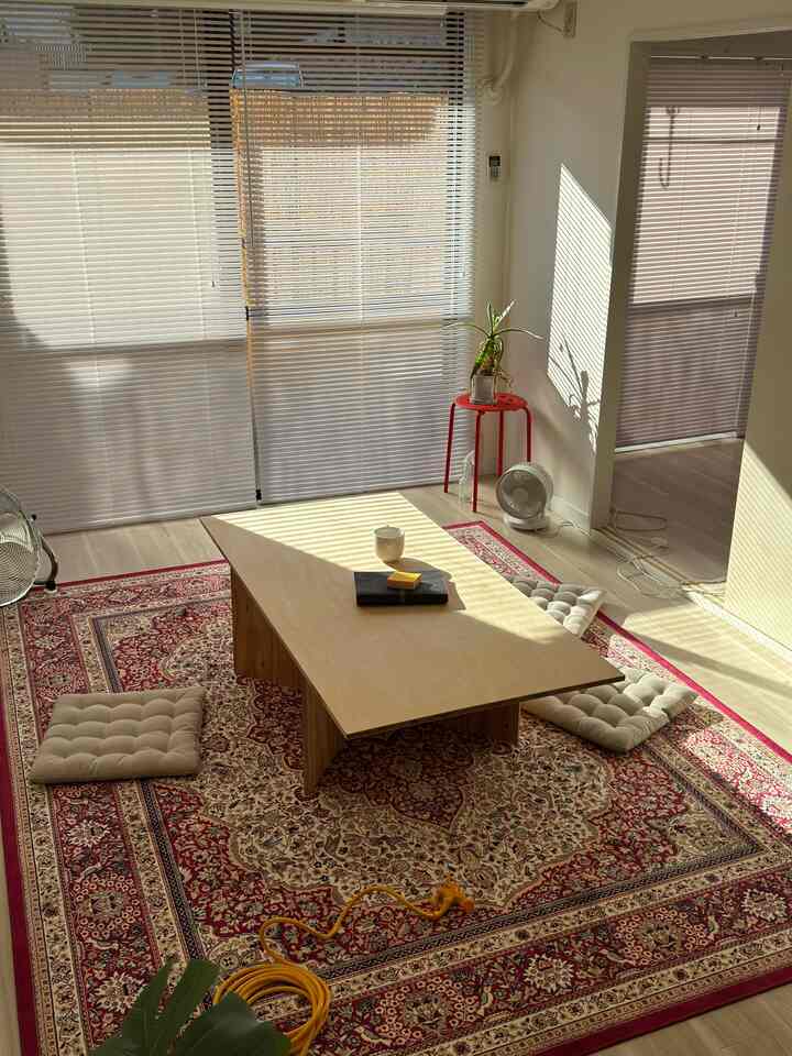 自然光が差し込む赤いペルシャ絨毯の上にベージュの座布団と木製のローテーブルが配置されたリビング