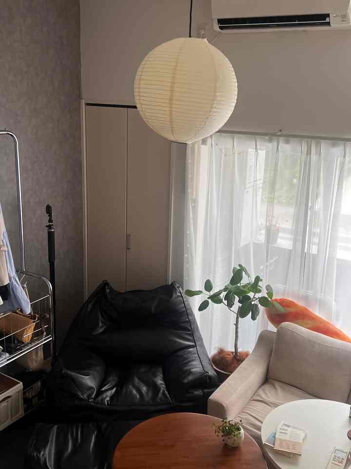 白い照明と黒のビーズクッションがある狭いワンルームのリビング、テーブルと植物が配置されたコンパクトな空間