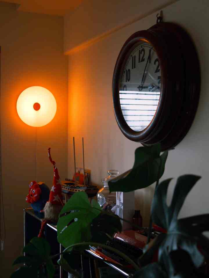 温かみのあるオレンジ色調のダイニング、ドーナツ型の間接照明とヴィンテージの壁時計が配置された雰囲気のあるインテリア