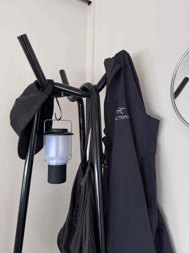 黒を基調とした玄関スペースに黒い金属製のコートハンガーと黒いジャケット、帽子が配置された実用的なインテリア