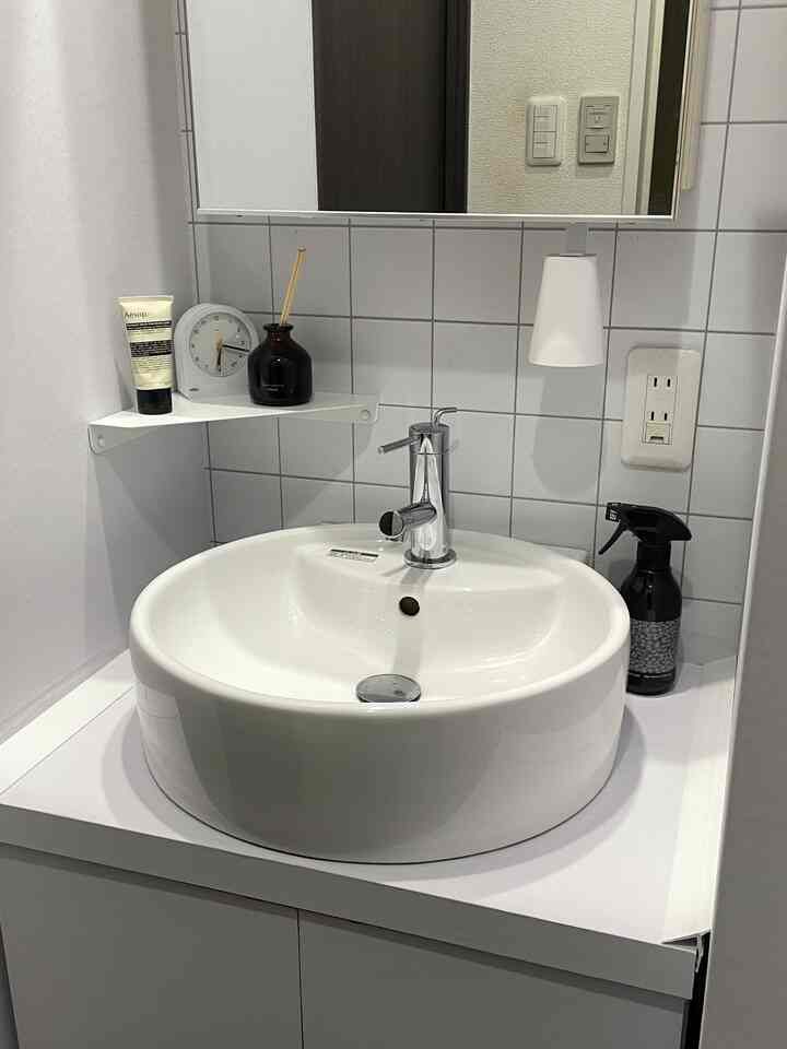 White-toned bathroom sink area featuring a round basin and a corner shelf with a simple and clean interior