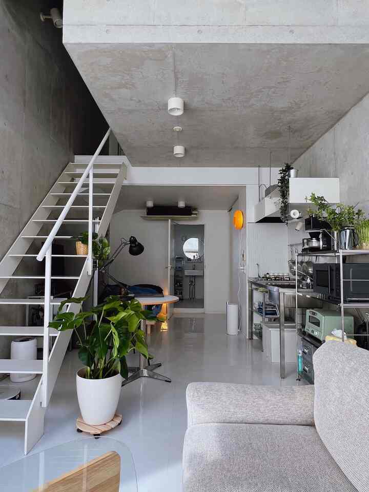 明るい灰色のソファと白い階段、金属製のキッチン家具と緑の植物が調和するミニマルモダンなロフトリビング空間