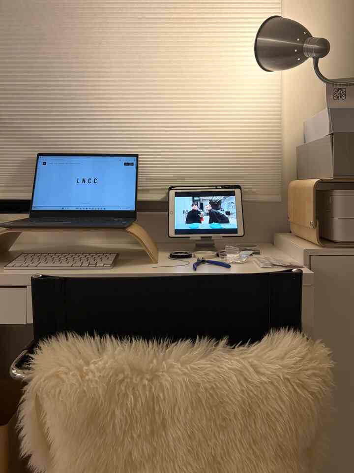Natural color and white compact single-person home office featuring wood tone accents, monitor stand, and desk lamp for functionality