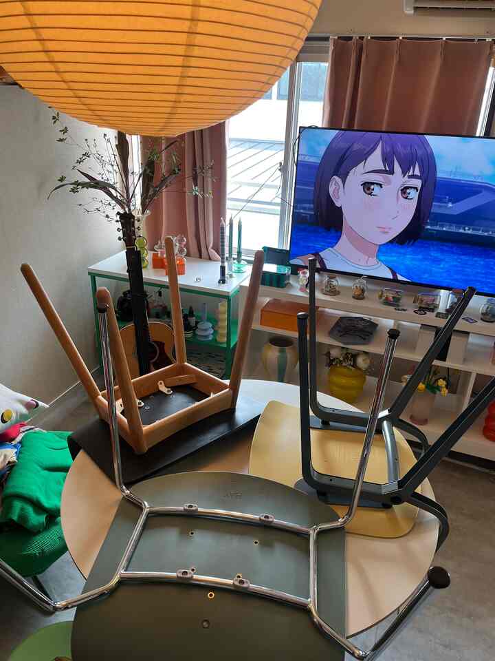 温かみのあるナチュラルトーンの1LDKリビング兼ダイニング、中央に逆さに置かれたダイニングテーブルと椅子が配置された印象的な空間