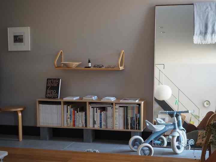 グレーの壁と天井の玄関、木目調の本棚とスツール、大きな鏡が配置されたミニマルで北欧風なインテリア