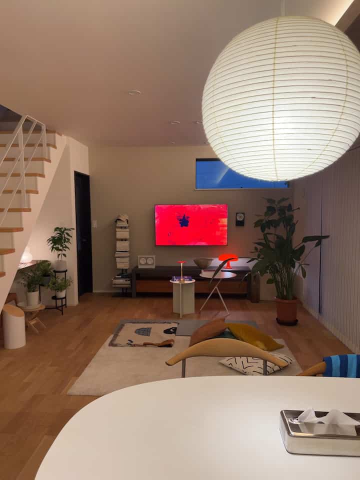 木目調と白が調和するミッドセンチュリーモダンのリビングルーム、大型のペンダントライトが中央に配された温かみのある空間