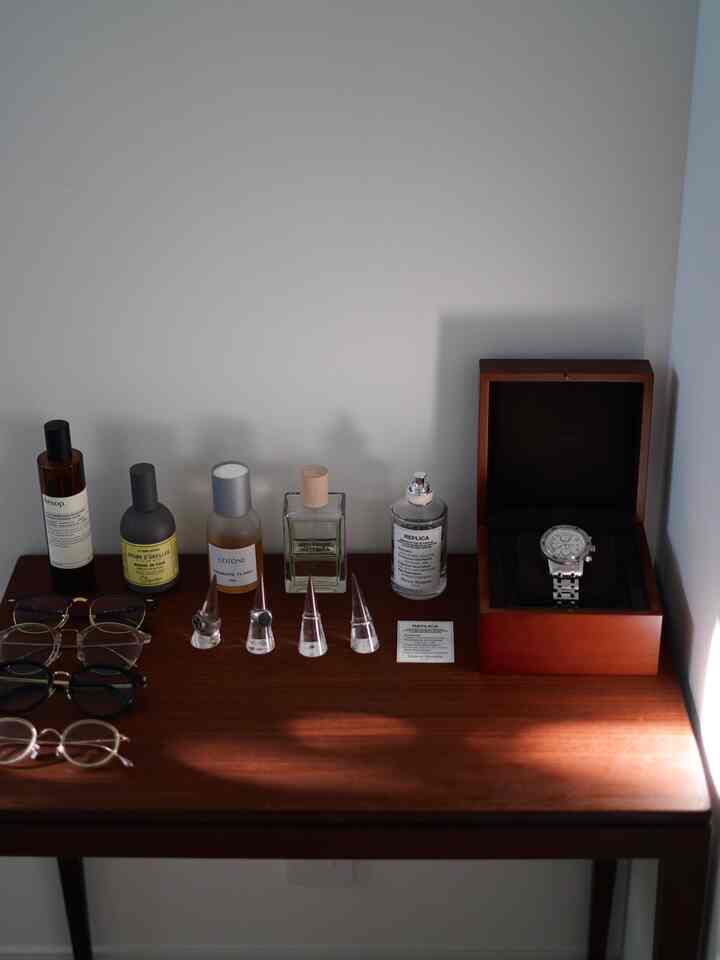 Natural wood tone table in an entrance area featuring perfumes, rings, and a watch with a simple arrangement