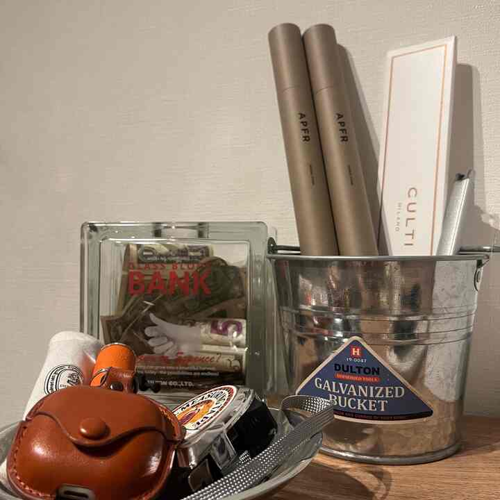 ナチュラルなベージュの壁と木製テーブルに、ガルバナイズドバケットやガラスの貯金箱などのインテリアアクセサリーが配置された印象的な空間