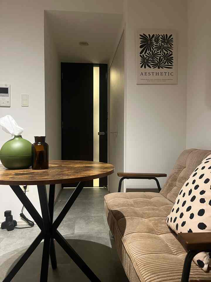 モノトーンと木目調の6畳1K空間、黒いアイアンテーブルとベージュのソファが配置されたモダンなカフェ風インテリア