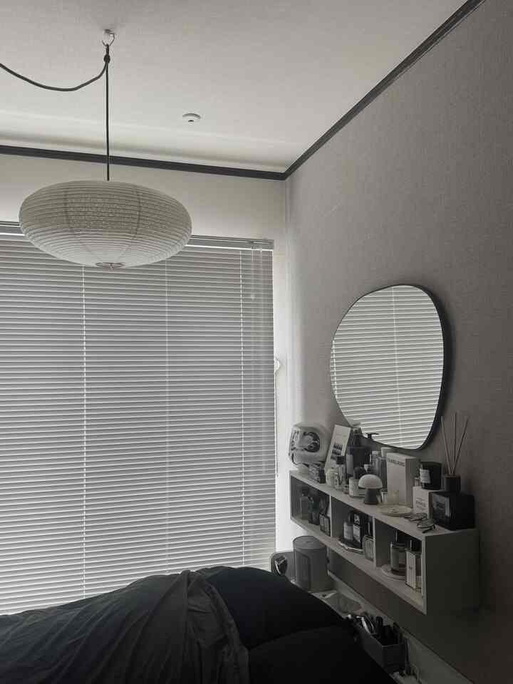 Natural tone bedroom featuring black bed, window blinds, a pendant light hanging from ceiling, and an oval mirror on the wall with tidy layout