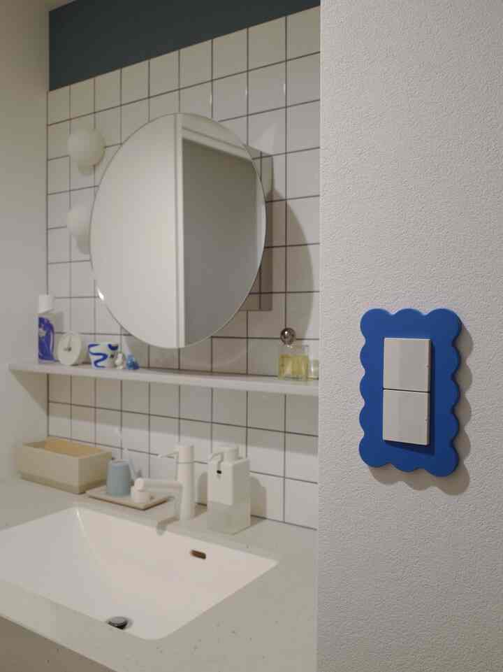 白と青の調和が取れたバスルーム、丸い鏡と洗面台、青いスイッチカバーが配置されたシンプルなインテリア