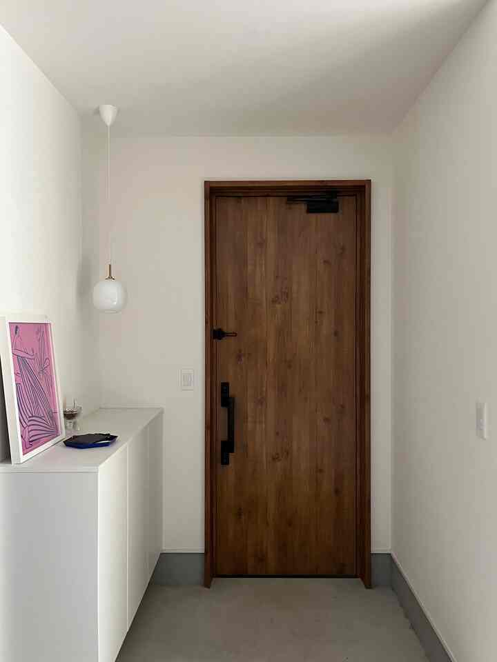 ナチュラルな白と木目調の玄関、シンプルな白い収納キャビネットとピンクのポスターが配置された清潔感のある空間