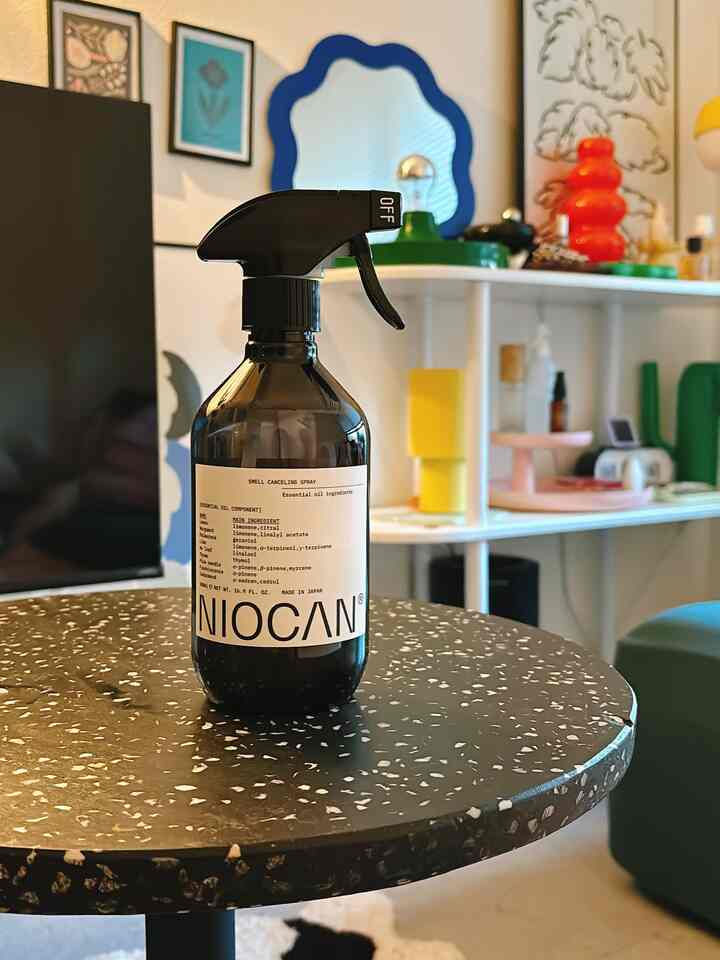 白と緑の色調が特徴の8畳ワンルーム、中央にサイドテーブルとモノトーンの消臭スプレーが置かれた洗練された空間