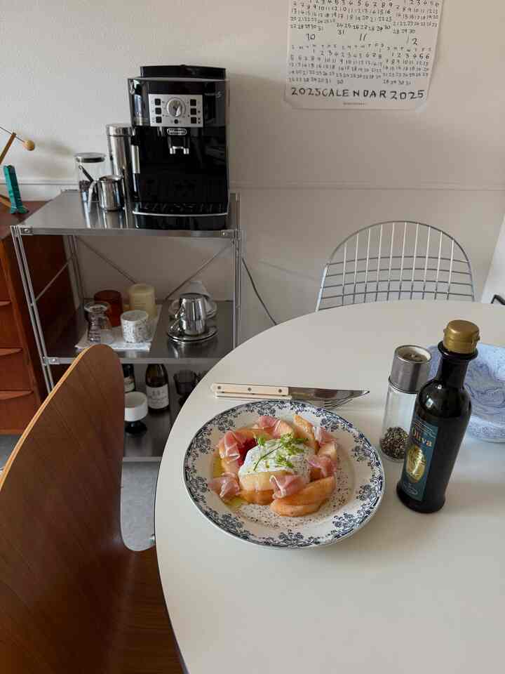 ホワイトとブラックのトーンが調和する1LDKのダイニングルーム、丸テーブルとコーヒーマシン、ステンレス棚が配置された雰囲気のあるおうちカフェ空間