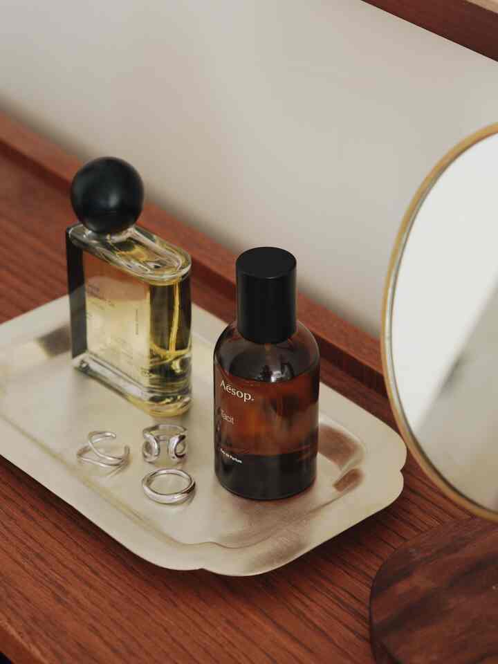 シルバーのトレイが置かれたウッドトーンのナイトテーブルとオーバルスタンドミラーが配置されたシンプルで温かみのあるインテリア