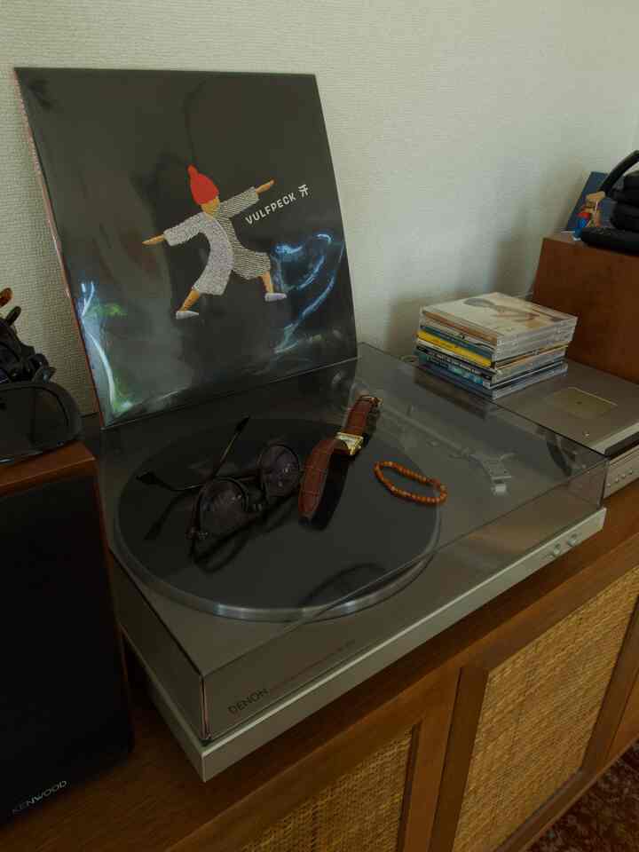 木製キャビネットの上にレトロなターンテーブルとビニールレコード、眼鏡と腕時計が置かれた雰囲気のあるインテリア