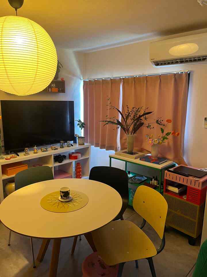 黄色と白を基調とした1LDKのリビング、丸いダイニングテーブルと異なる椅子が配置されたミッドセンチュリーモダン様式の空間