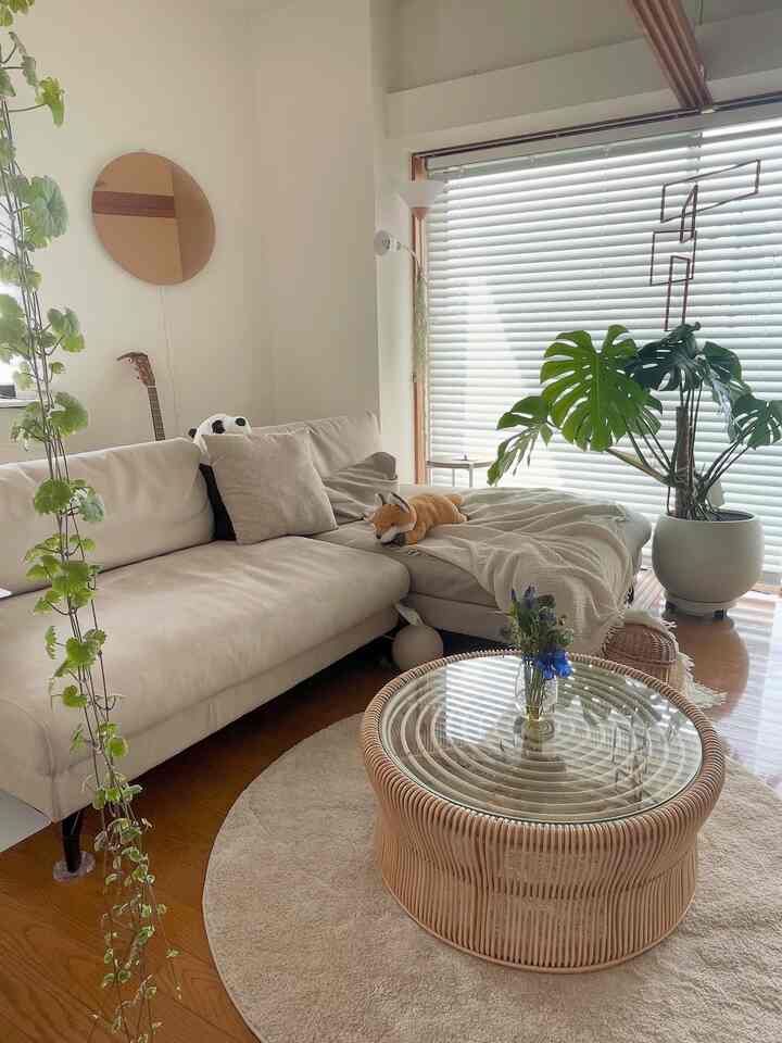 白とベージュの色調のリビング、自然素材のソファとラタンの円形コーヒーテーブル、モンステラの植物が配置された雰囲気のあるインテリア