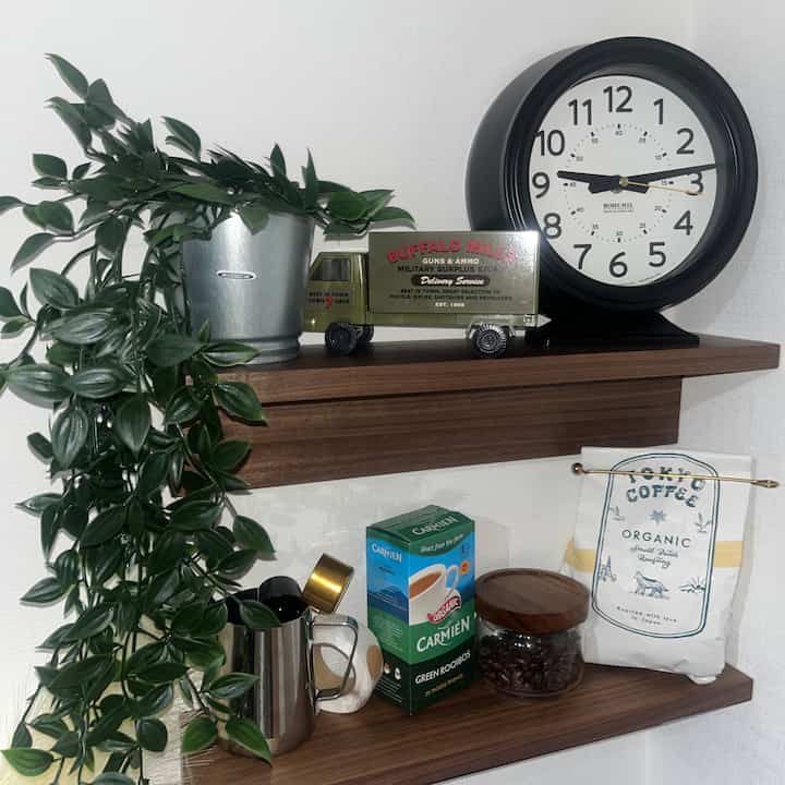 Natural brown wood tone wall shelves featuring clock, metal pot with artificial plant in a cozy home cafe corner