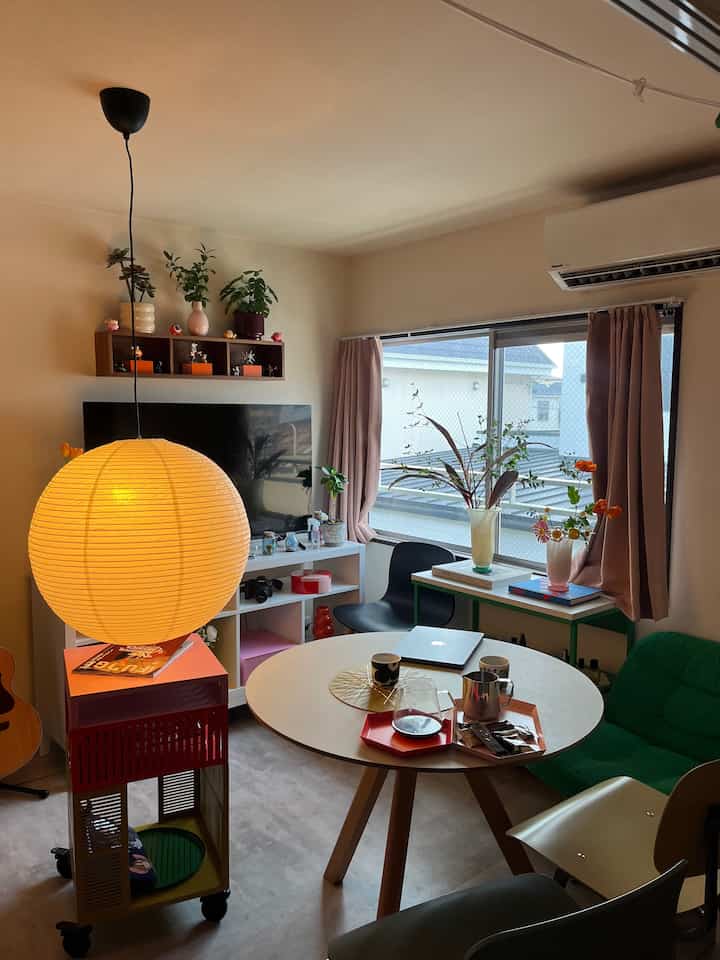 白い壁とグリーンのソファ、丸いダイニングテーブルと和紙の照明が配された1LDKのミッドセンチュリーモダンなリビング