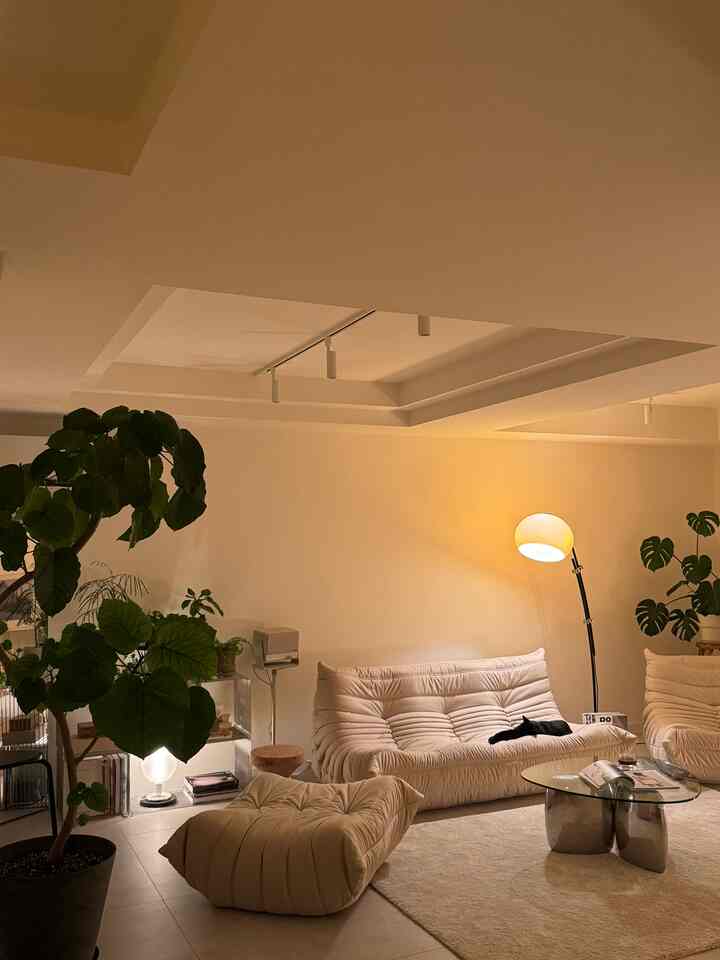 暖かい黄色のトーンが調和したナチュラルなリビング、ベージュのソファとラグ、植物が配置され、雰囲気のある空間