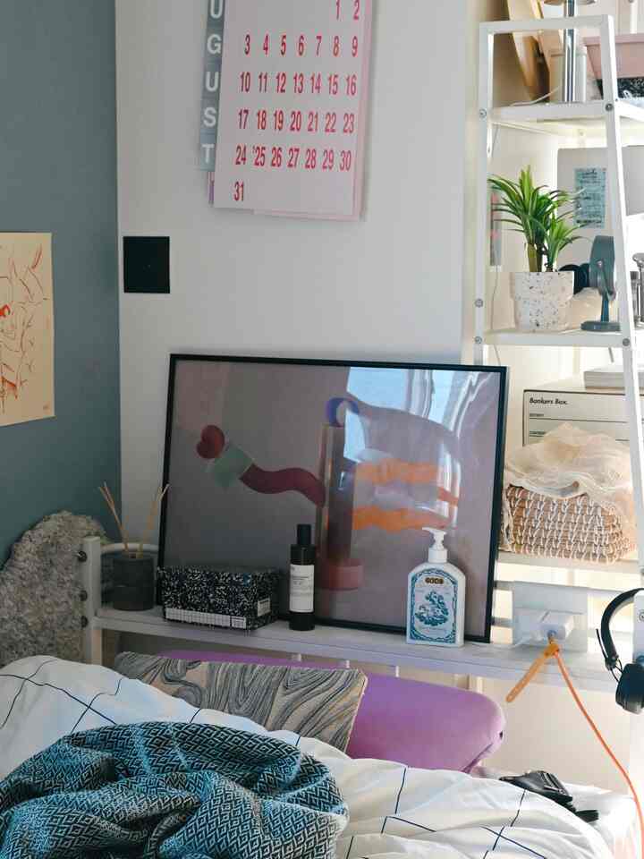White-walled bedroom with blue patterned bedding, poster and storage baskets arranged in a cluttered space