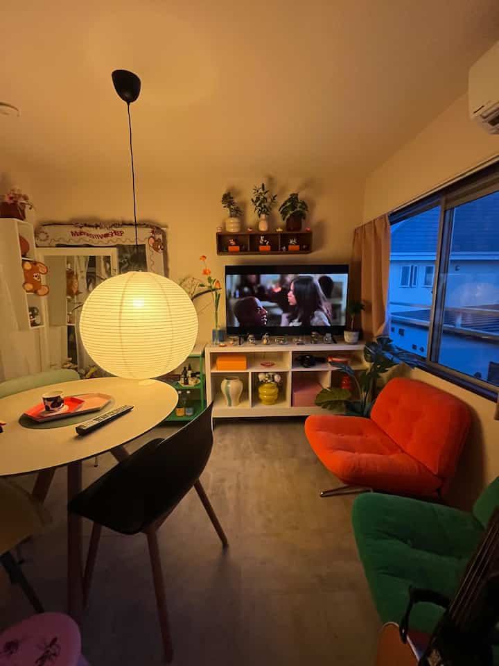 温かみのあるオレンジとグリーンのアームチェアが配置された1LDKのリビング、丸いペンダントライトが印象的なカラフルな空間