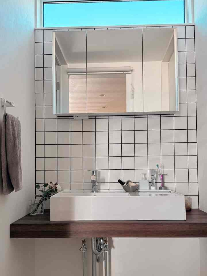 明るい白いタイル壁とブラウンの木目調洗面台が調和した、自然な雰囲気のあるバスルーム