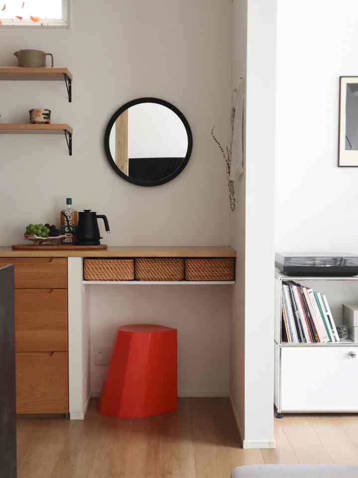 ラタンのバスケットと赤いスツールがある白い壁面のリビング、ナチュラルで落ち着いた雰囲気のインテリア