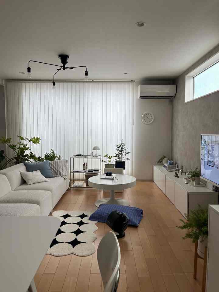 White and wood tone living room featuring a simple sofa, round coffee table, and green plants with a natural atmosphere