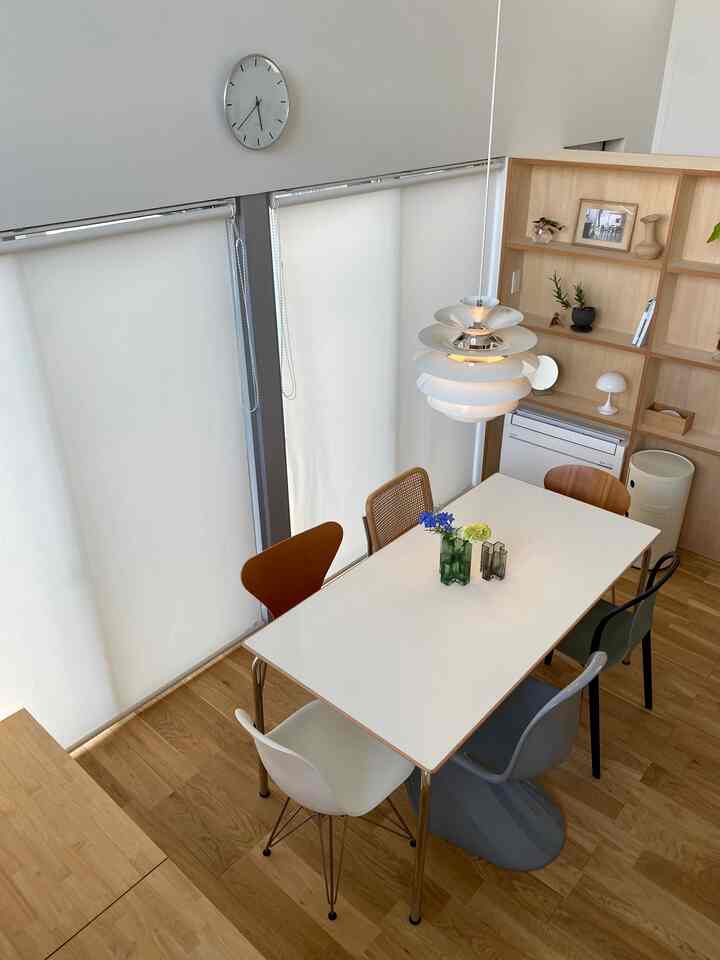 白とナチュラルウッド調が調和したダイニングルーム、多様なチェアと洗練されたペンダントライトが配置されたモダンな空間