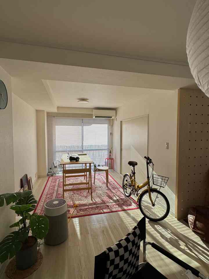 やわらかな白い色調のバルコニー空間に赤いペルシャ絨毯、木製ダイニングテーブル、黄色い自転車が配置された雰囲気のある多目的ルーム