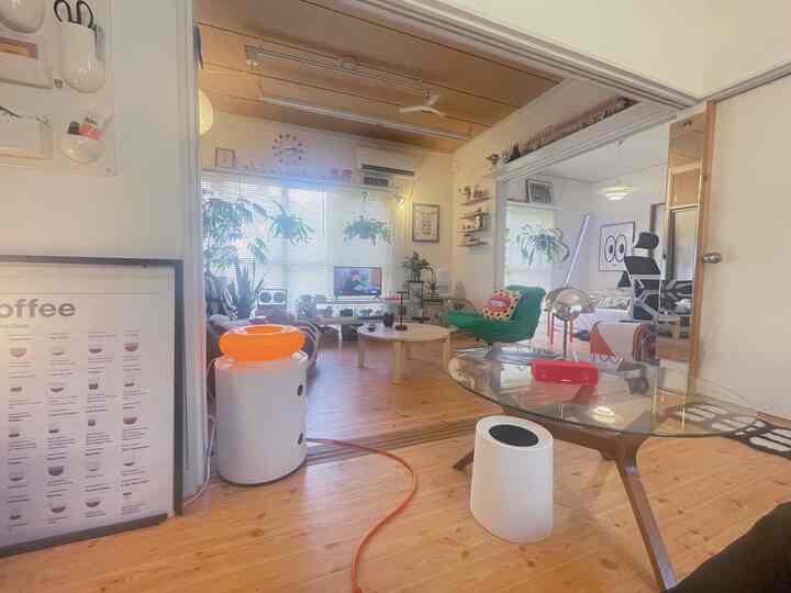 ナチュラルな木目調と白いトーンのワンルームリビングと寝室がつながった空間、緑のアームチェアと植物が配置された雰囲気のあるインテリア